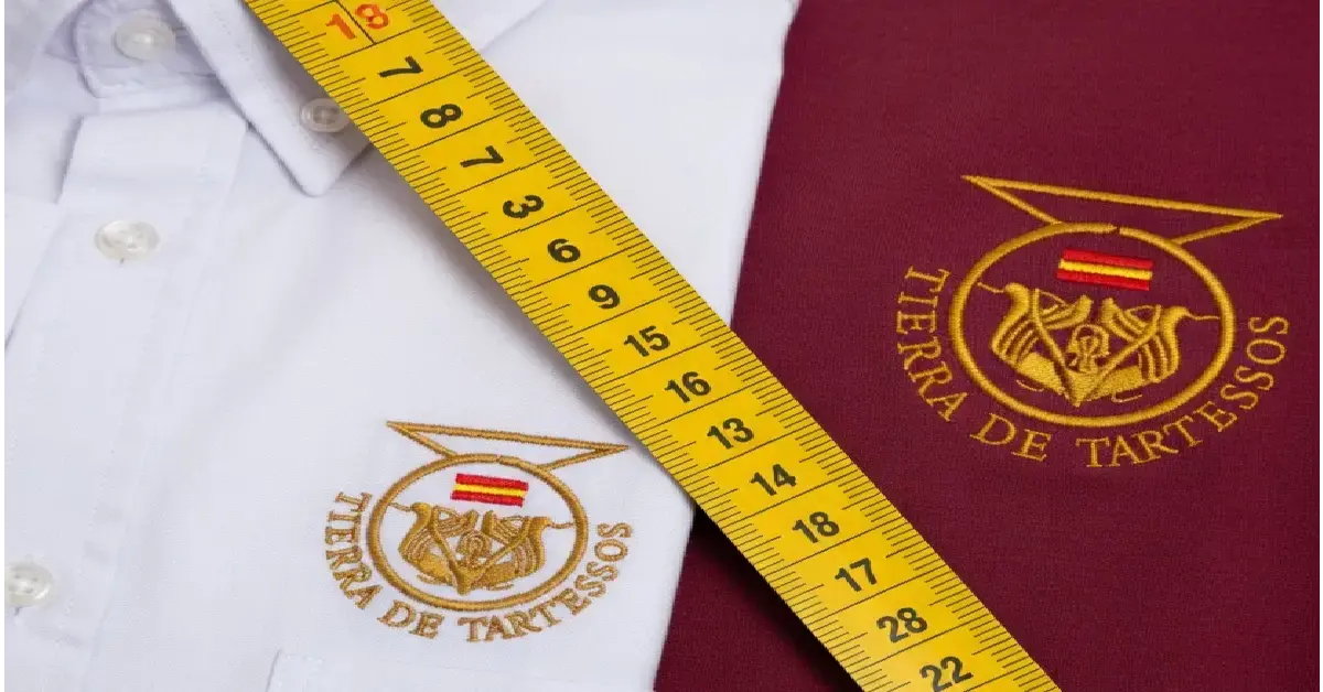 Guía de tallas unisex de Tierra de Tartessos con metro de costura sobre camisas blancas con logo dorado.
